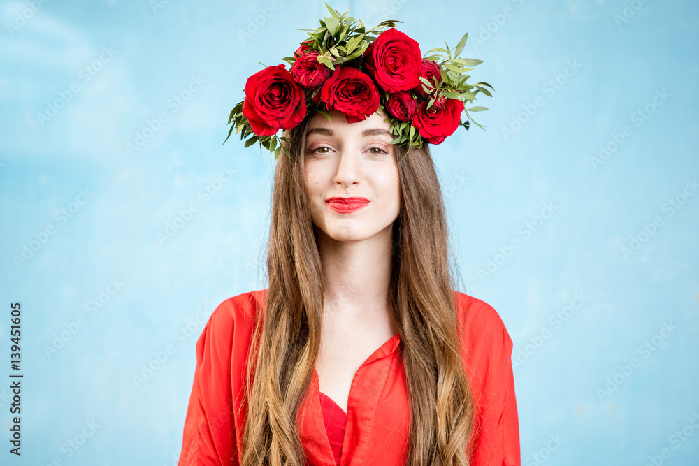 Colorful portrait of a beautiful woman in red dress with wreath made of red roses on the blue backgr