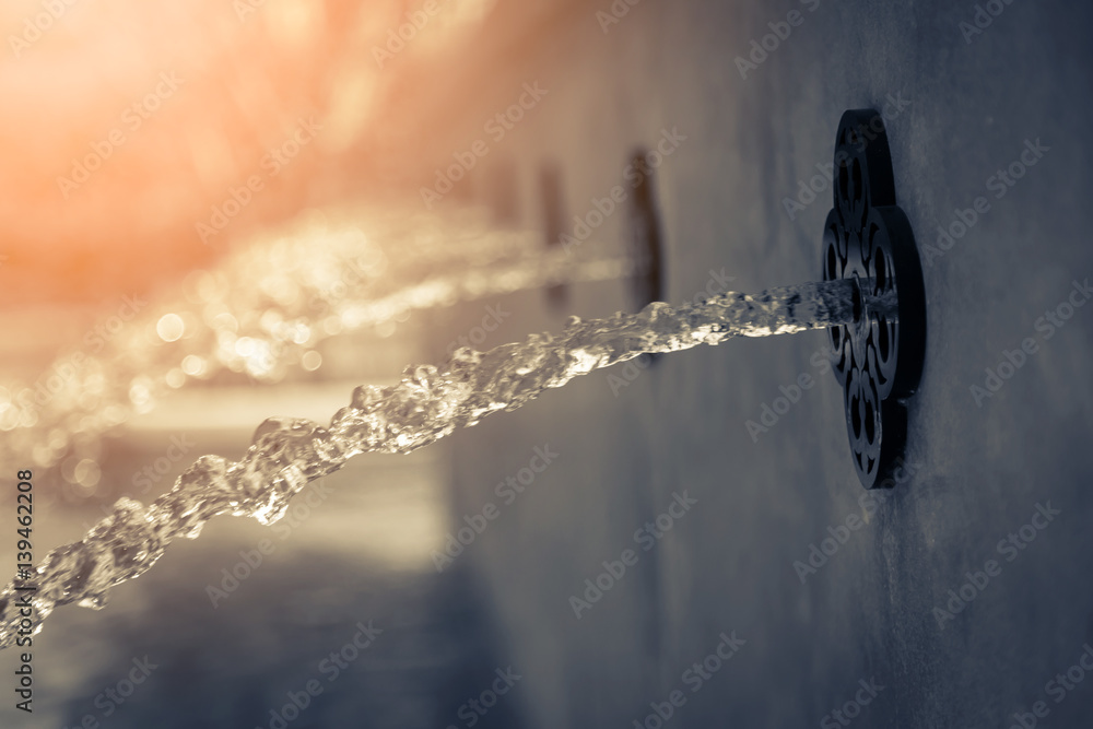 water flow from fountain from red wall cement decorstion pool with tree bokeh background