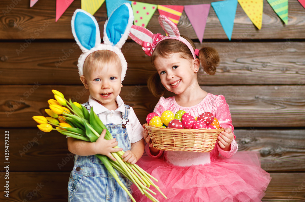 Happy kids boy and girl dressed as Easter bunnies with basket of eggs and flowers .