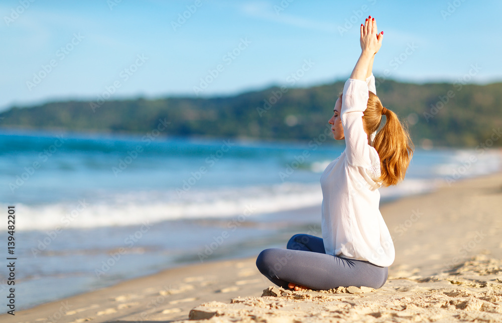 woman practices yoga and meditates in lotus position on beach