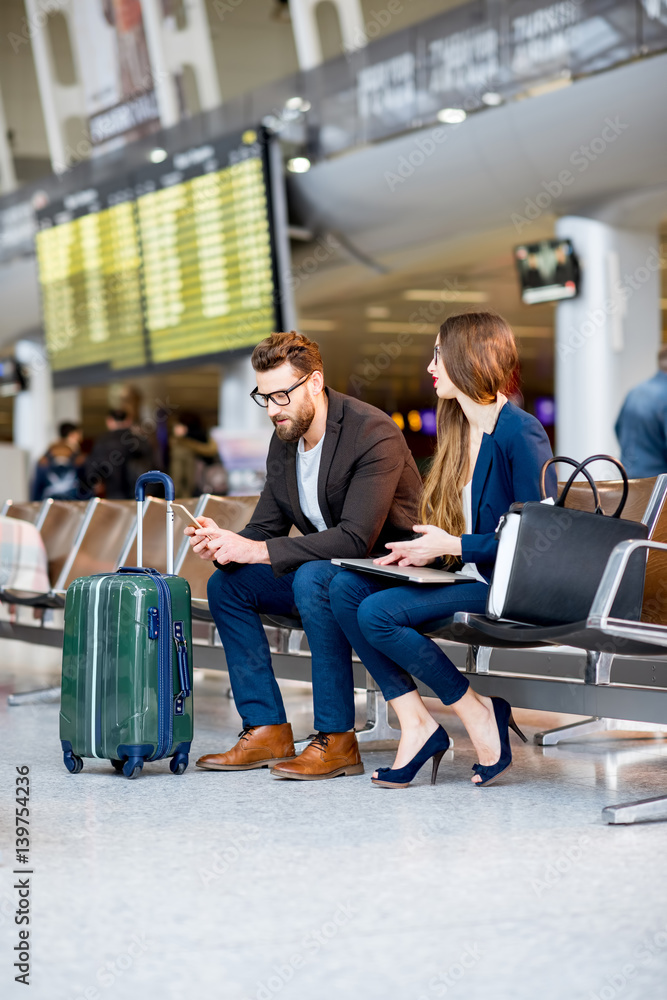 优雅的商务情侣坐在机场候机厅，拿着电话和预订。商务旅行