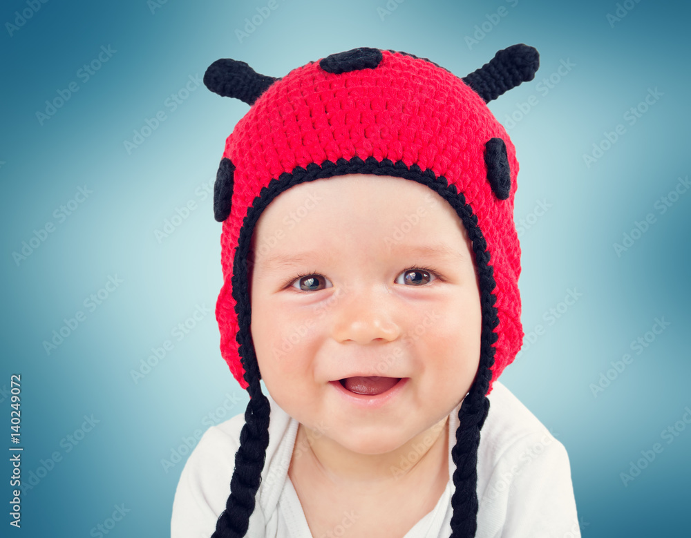 Cute baby lying in the bed on white blanket in ladybug hat