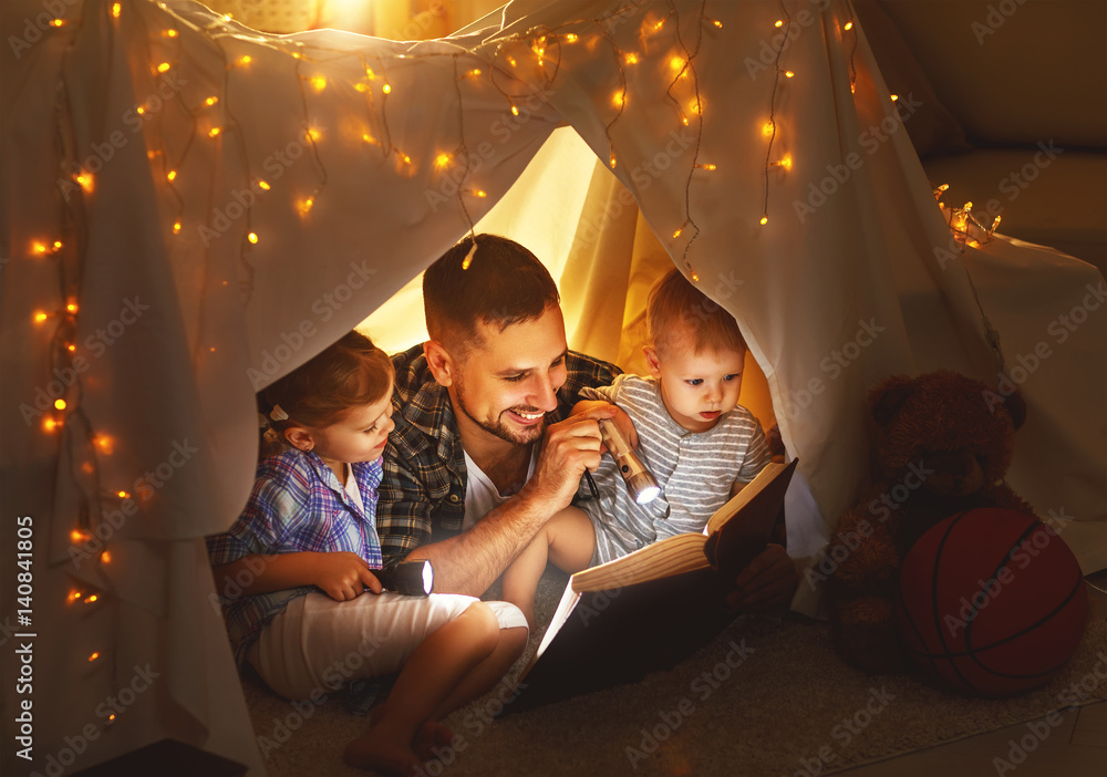 幸福的家庭父亲和孩子在家里的帐篷里看书