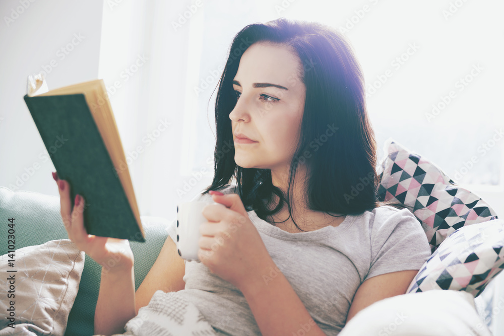 放松的女人在家喝咖啡看书
