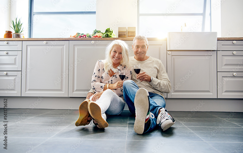 Laughing mature couple holding wine in kitchen