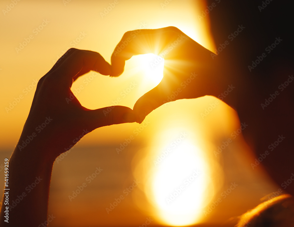 Hands in shape of heart at sunset on beach
