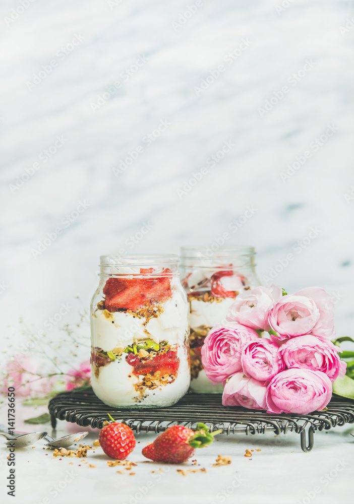 健康的春季早餐。希腊酸奶、格兰诺拉麦片、罐装新鲜草莓早餐、粉色raninkulus
