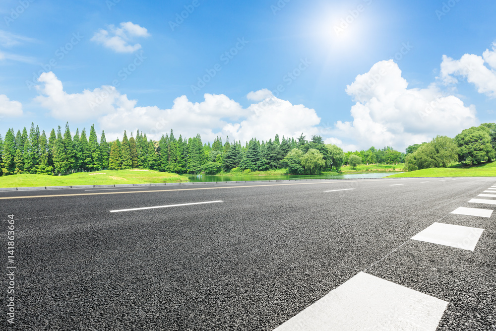 Asphalt road and green trees in the blue sky