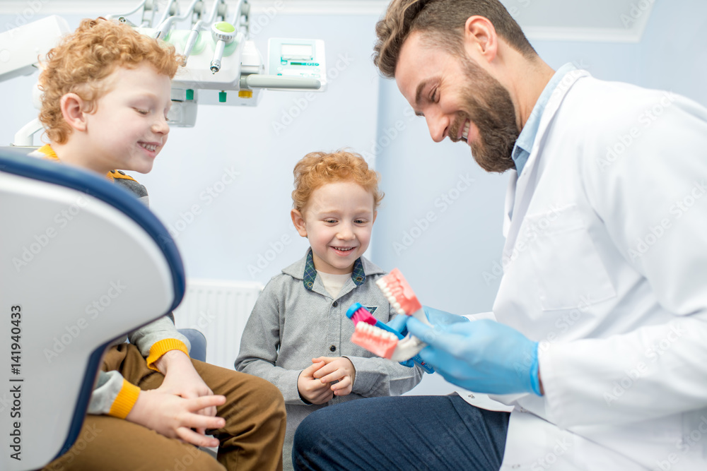 儿童牙医在牙科诊所向男孩们展示如何在人工下颌上刷牙