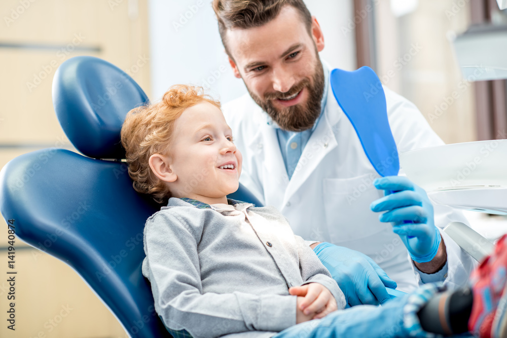 年轻兴奋的男孩坐在椅子上看着牙科镜子，牙医在牙科诊所