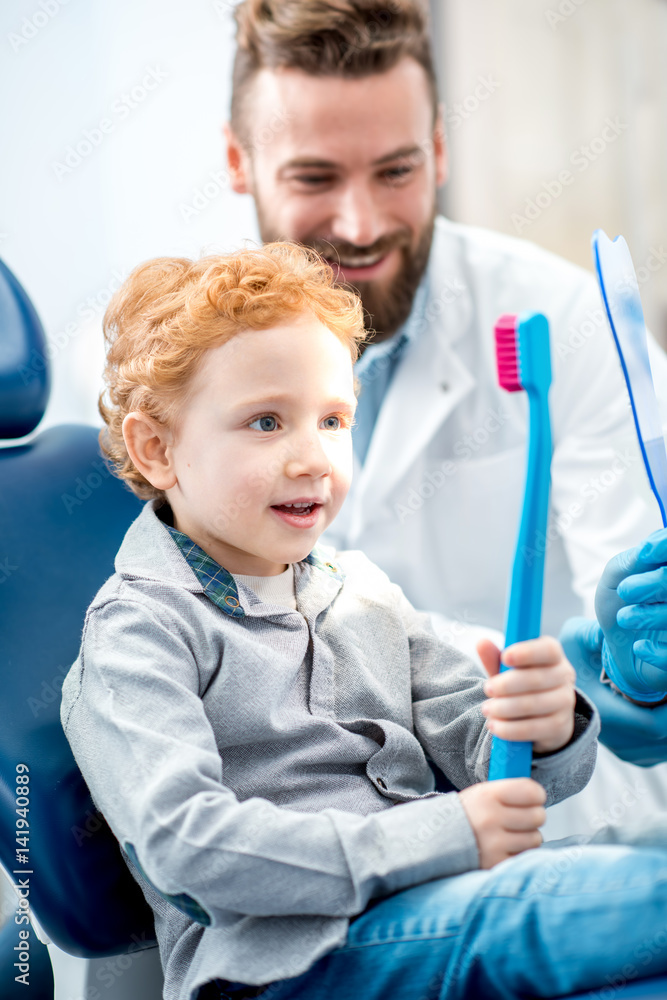 年轻兴奋的男孩坐在椅子上，手里拿着大牙刷，和医生在牙科办公室