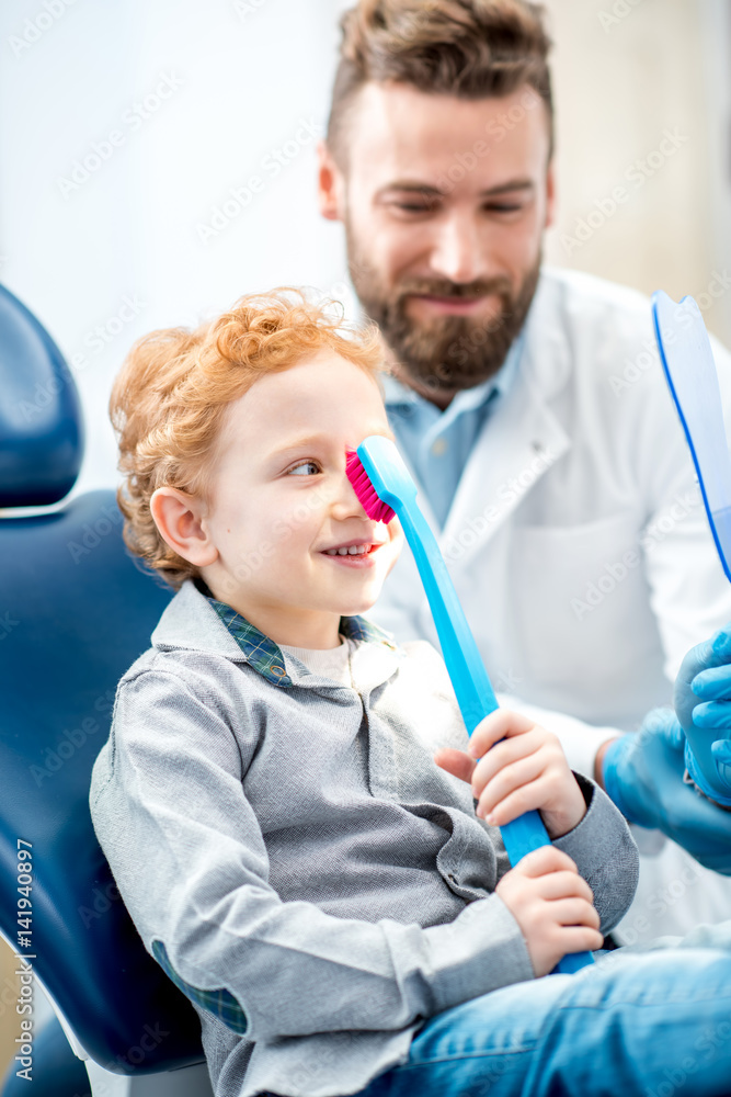 年轻兴奋的男孩坐在椅子上，手里拿着大牙刷，和医生在牙科办公室
