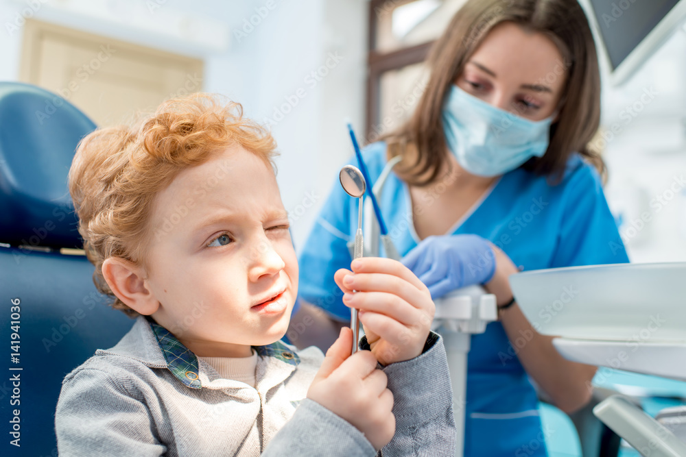 年轻兴奋的男孩看着牙科镜子，坐在椅子上，牙医在牙科诊所