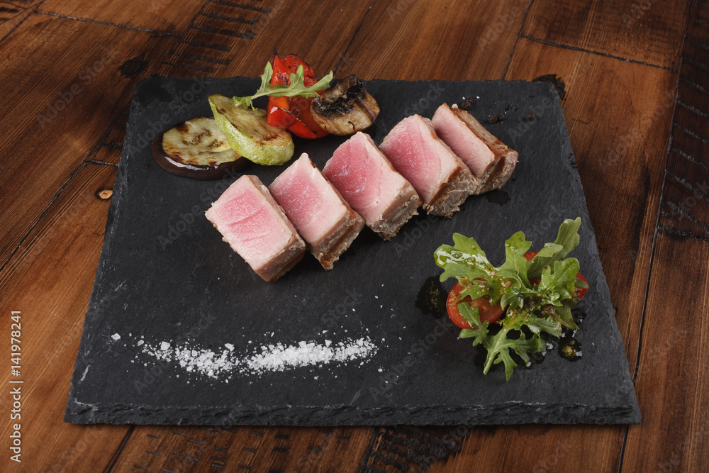 Tuna fillet slices with salad on gray slate. Cold fish appetizer. Wooden background