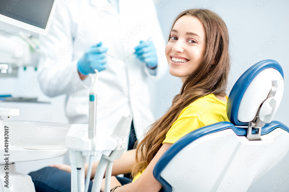 一位面带笑容的女士坐在牙科椅旁，背景是医生，照片位于t处