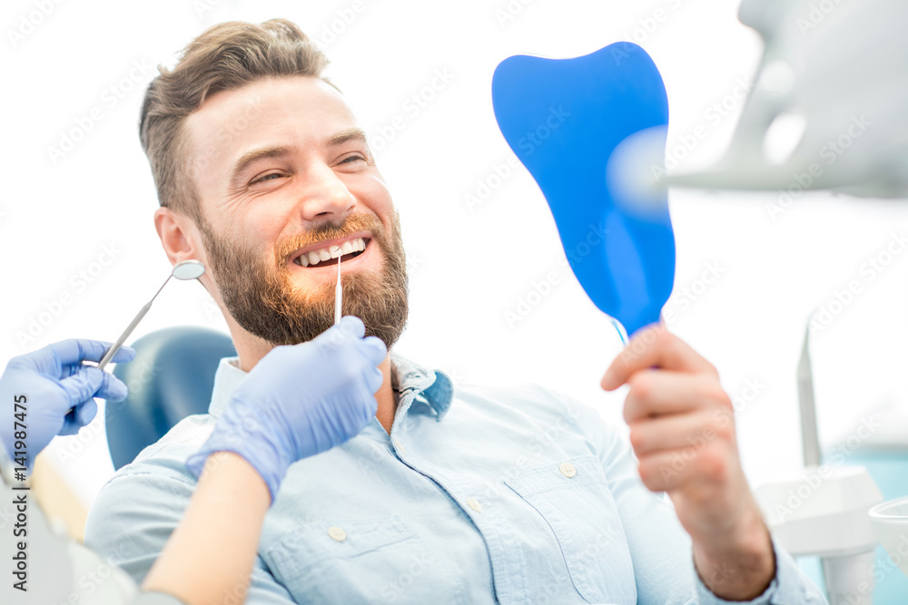 英俊的男性患者坐在牙科诊所，看着他美丽的笑容
