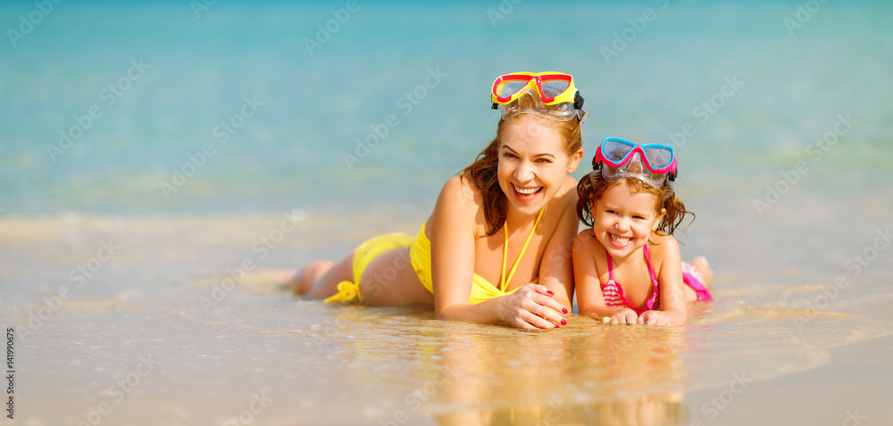 Happy family mother and chid daughter in masks on beach in summer