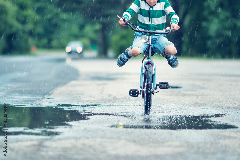 夏天孩子在柏油路上骑自行车。雨天公园里的自行车穿过水坑
