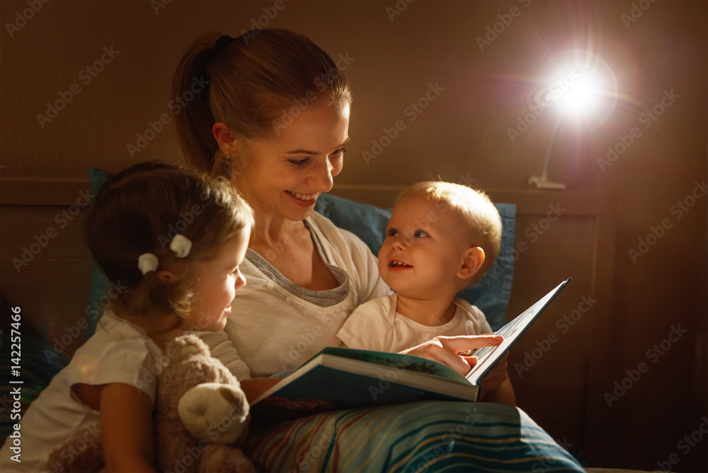 mother reads to children book in bed