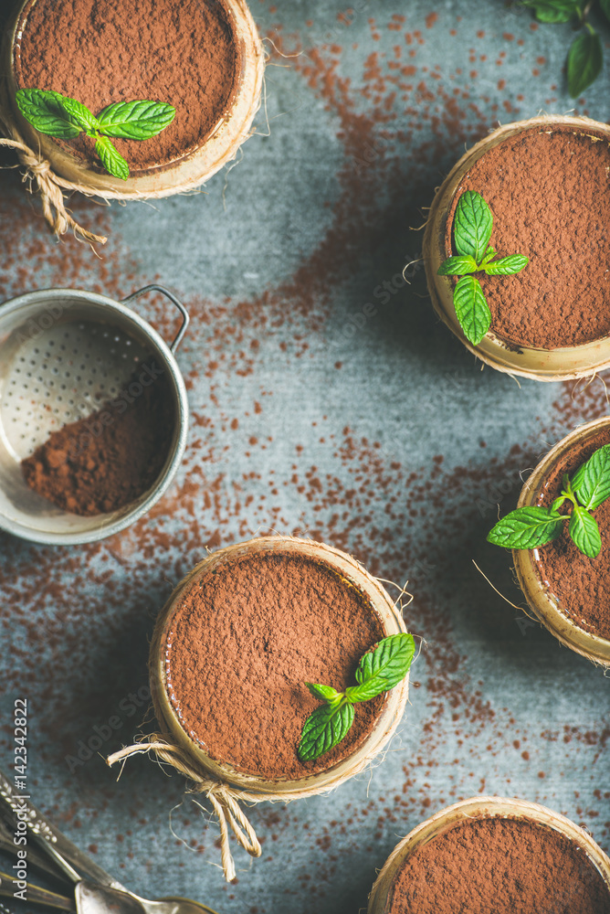 Homemade Italian dessert Tiramisu served in individual glasses with mint leaves and cocoa powder ove