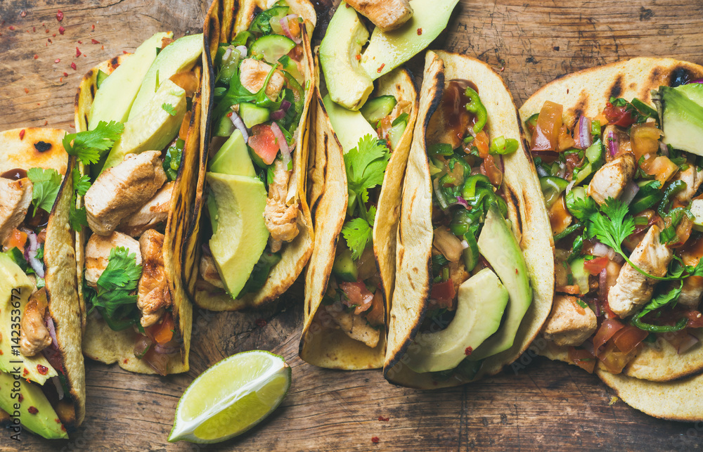Tacos with grilled chicken, avocado, fresh salsa sauce and limes over rustic wooden background, top 
