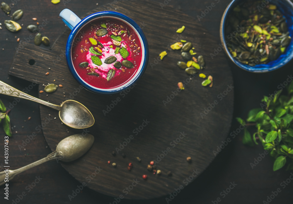 Spring beetroot soup with mint, pistachio, chia, flax, pumpkin seeds in blue enamel mug over dark wo