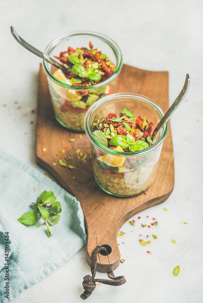 Healthy salad with quionoa, avocado, dried tomatoes, basil, olive oil, mint in glass jars on wooden 