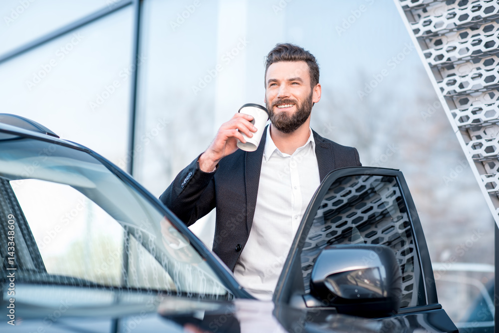 一位优雅的商人拿着咖啡杯站在汽车附近的肖像