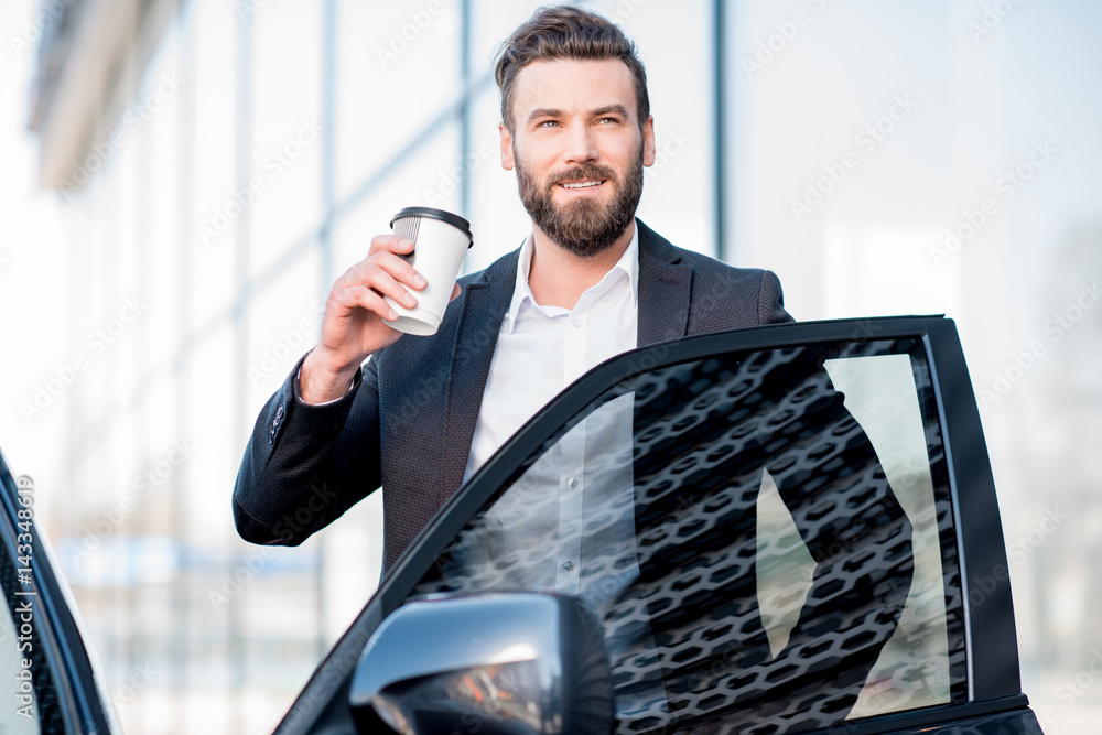一位优雅的商人拿着咖啡杯站在汽车附近的肖像