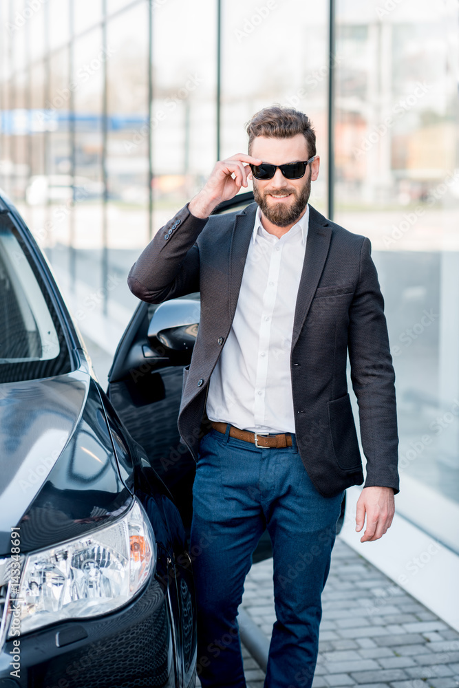一位戴着墨镜的英俊商人站在户外汽车附近的肖像