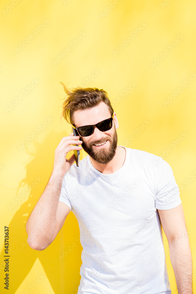 一个穿着白色t恤的英俊男子在黄色背景上与电话交谈的彩色肖像