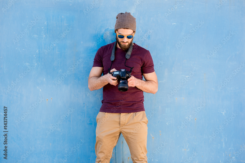 一位时尚摄影师的肖像，穿着休闲的t恤，戴着帽子，站在画布上拿着相机