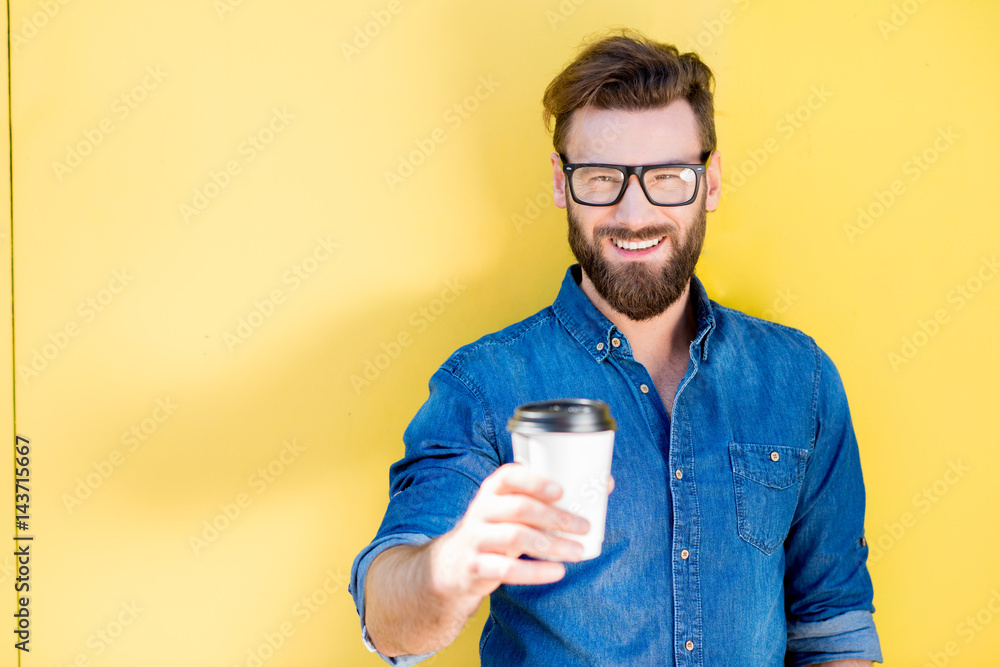 一个穿着蓝色t恤的英俊男子的肖像，站在黄色背景上喝咖啡