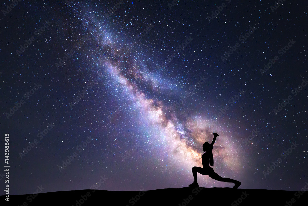 银河系，一个站着的女人在山上练习瑜伽的剪影。美丽的风景w