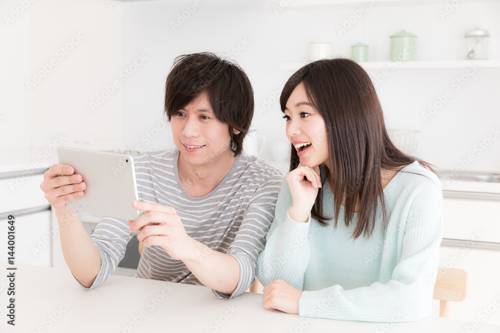 年轻的亚洲夫妇在厨房使用智能手机