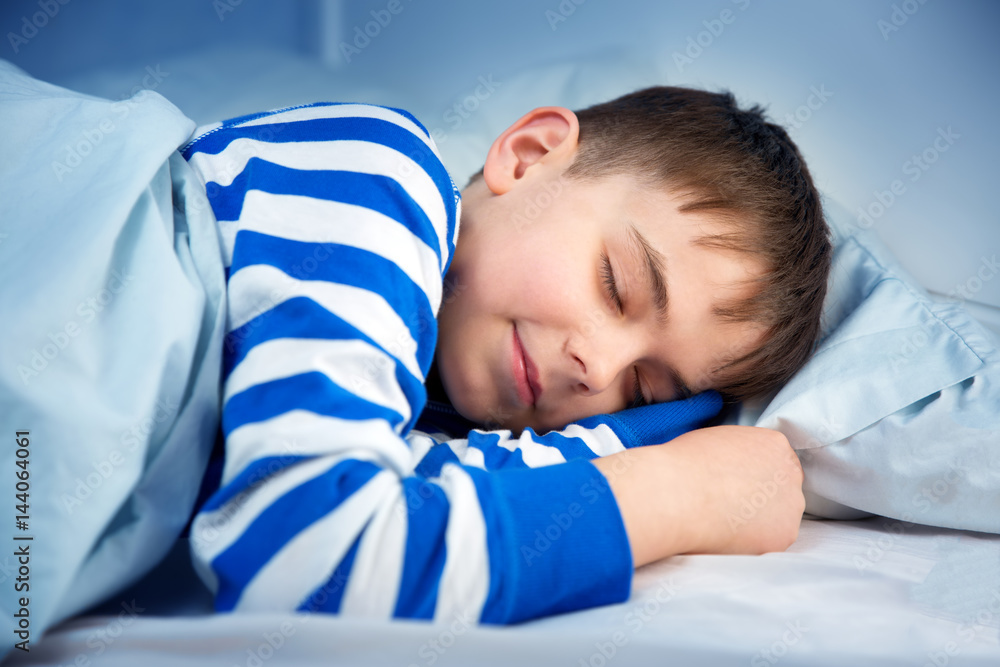 男孩穿着睡衣睡在床上。孩子晚上躺在床上的枕头上