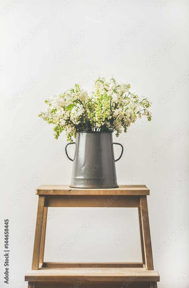 春天的一束白丁香，装在复古的灰色搪瓷花瓶里，后面是白色的墙背景