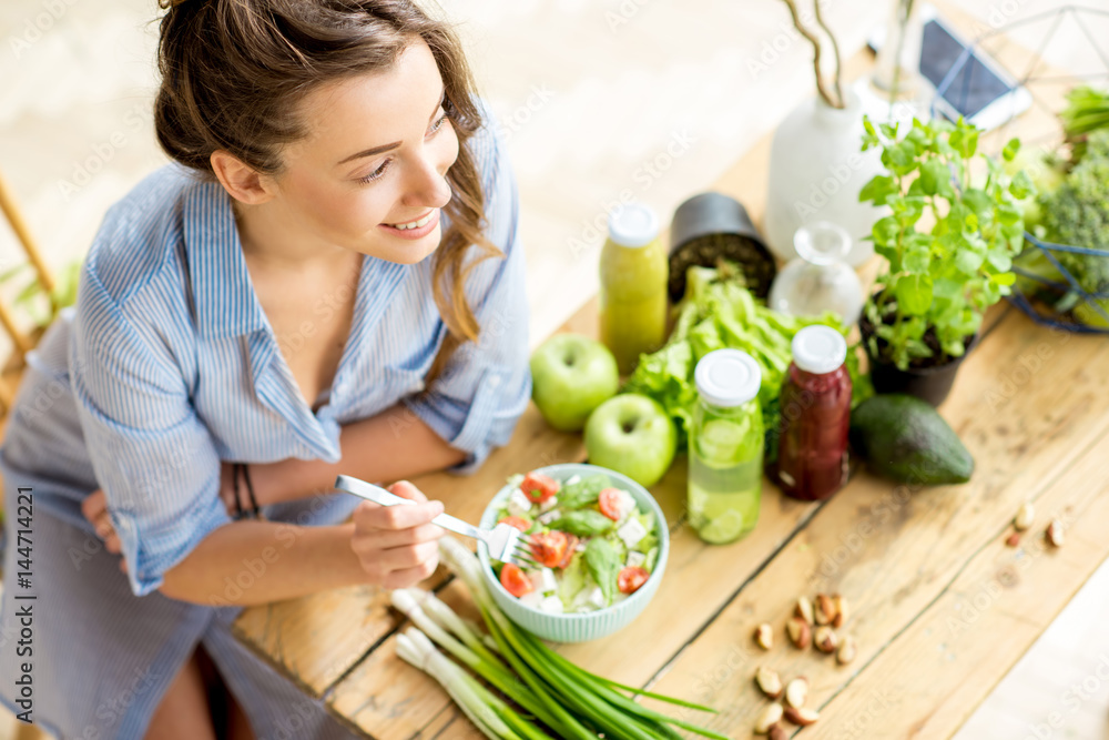 年轻快乐的女人在室内用绿色新鲜食材坐在桌子上吃健康沙拉