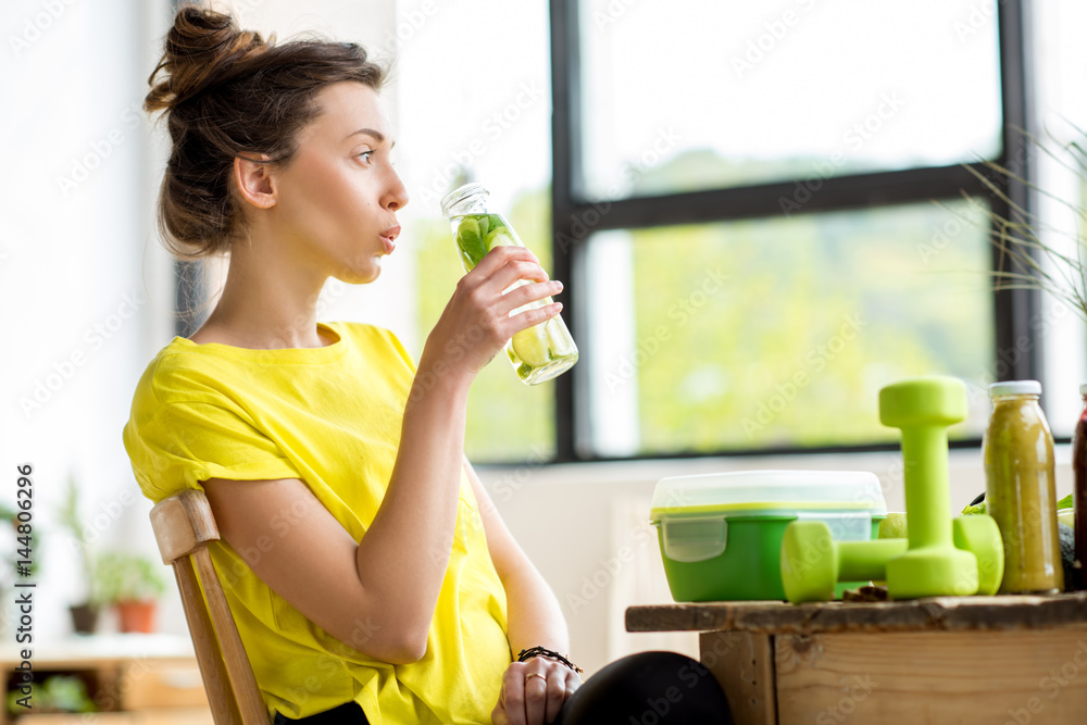 穿着黄色t恤的年轻运动女性饮用薄荷和黄瓜水。排毒概念