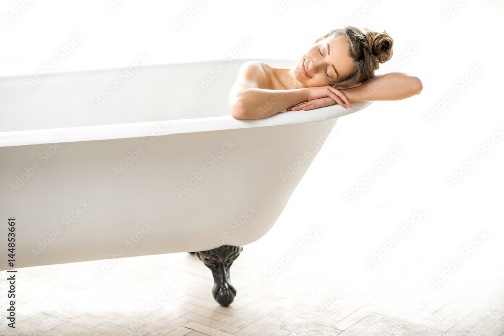 美丽的年轻女子躺在白色浴室的复古浴缸里放松