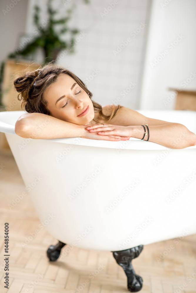 美丽的年轻女子躺在浴室的浴缸里放松