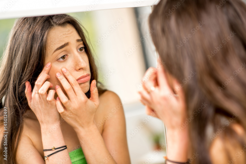 年轻悲伤的女人在浴室里看着镜子挤痘痘