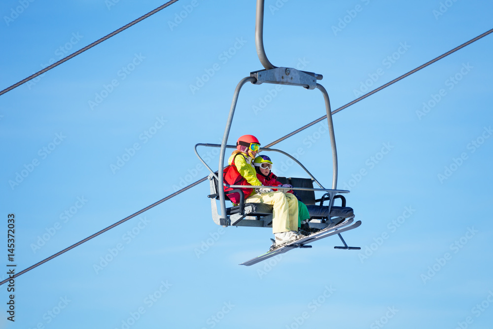 Two skiers lifting on chairlift against blue sky