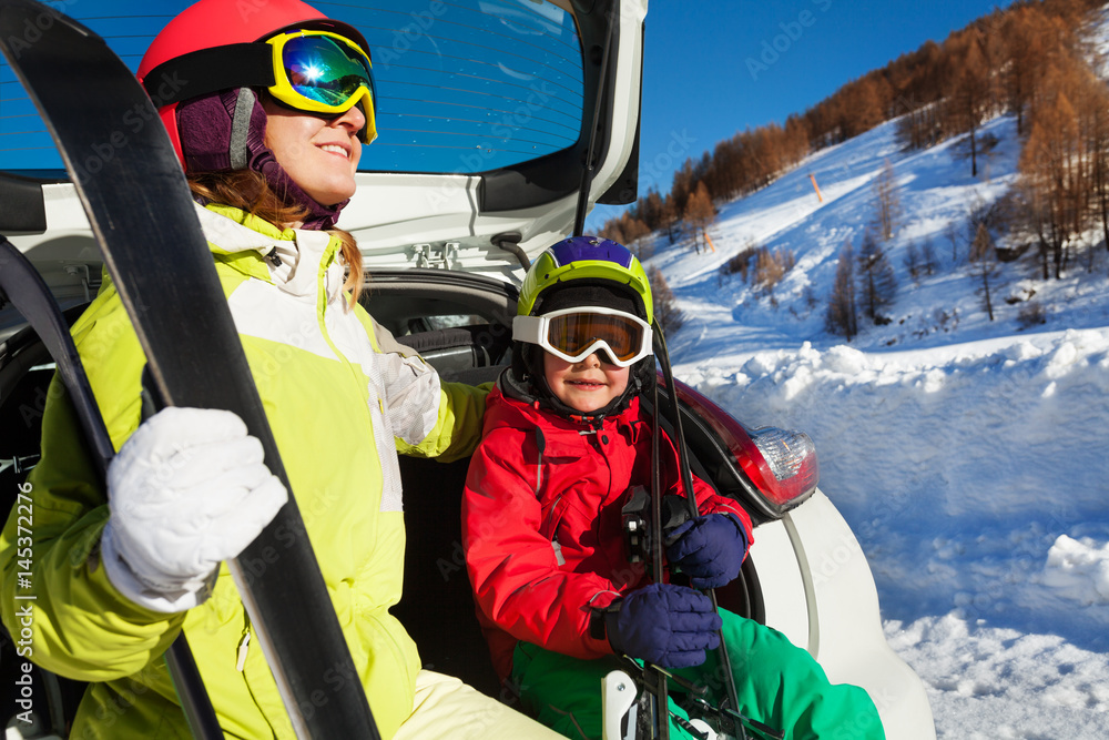 穿着滑雪服的女人和儿子坐在汽车后备箱上