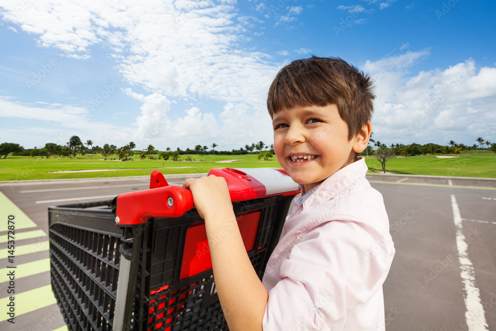 Smiling boy pushing the shopping cart at crosswalk