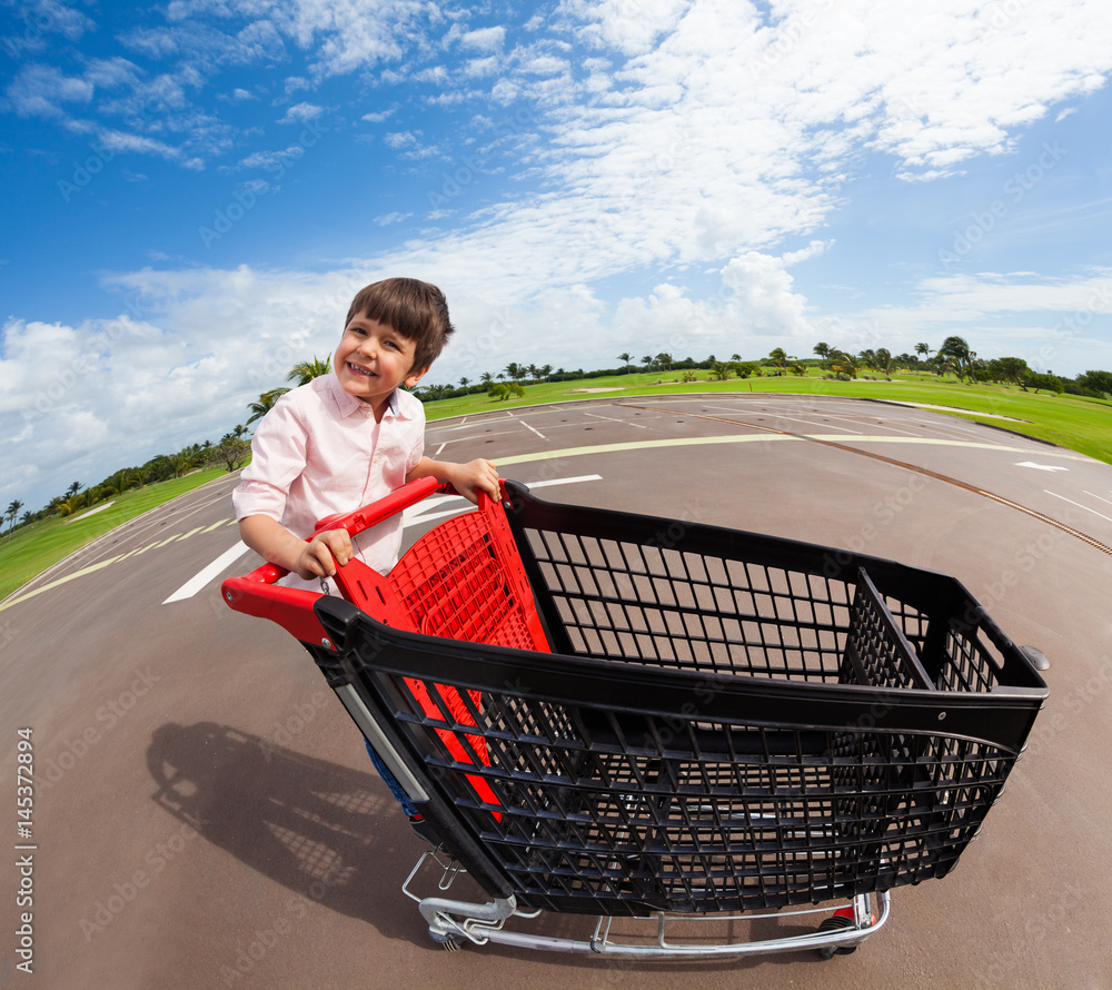 Happy boy riding empty supermarket shopping cart