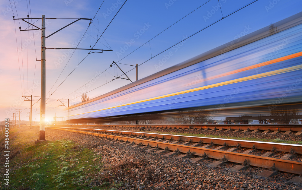 High speed passenger train in motion on railroad at sunset. Blurred commuter train. Railway station 