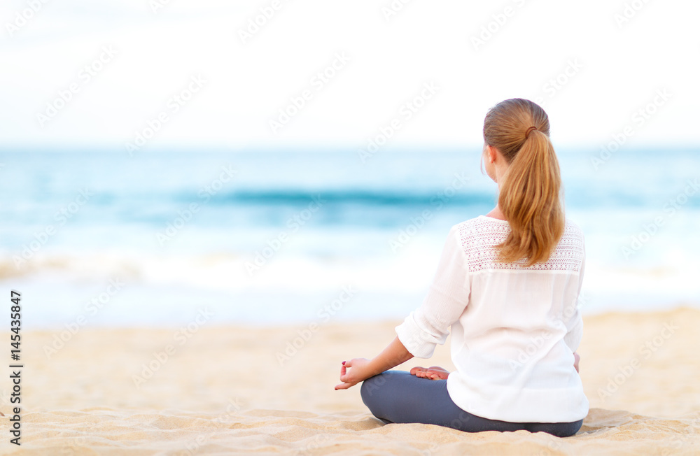 一位女士在海滩上练习瑜伽并以莲花姿势冥想。