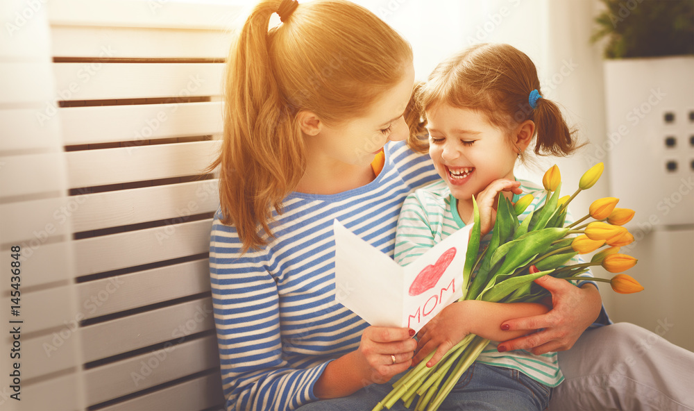 Happy mothers day! Child daughter congratulates moms and gives her a postcard and flowers