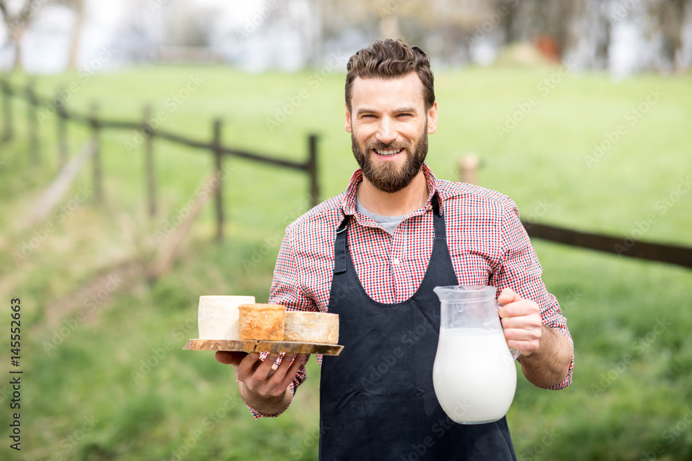 一个穿着围裙的英俊农民的画像，站在户外的绿色美阿上，手里拿着山羊奶酪和牛奶